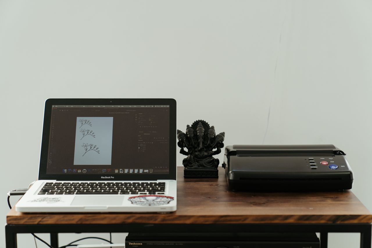 who-we-are A creative home office setup featuring a laptop, printer, and artistic design work.