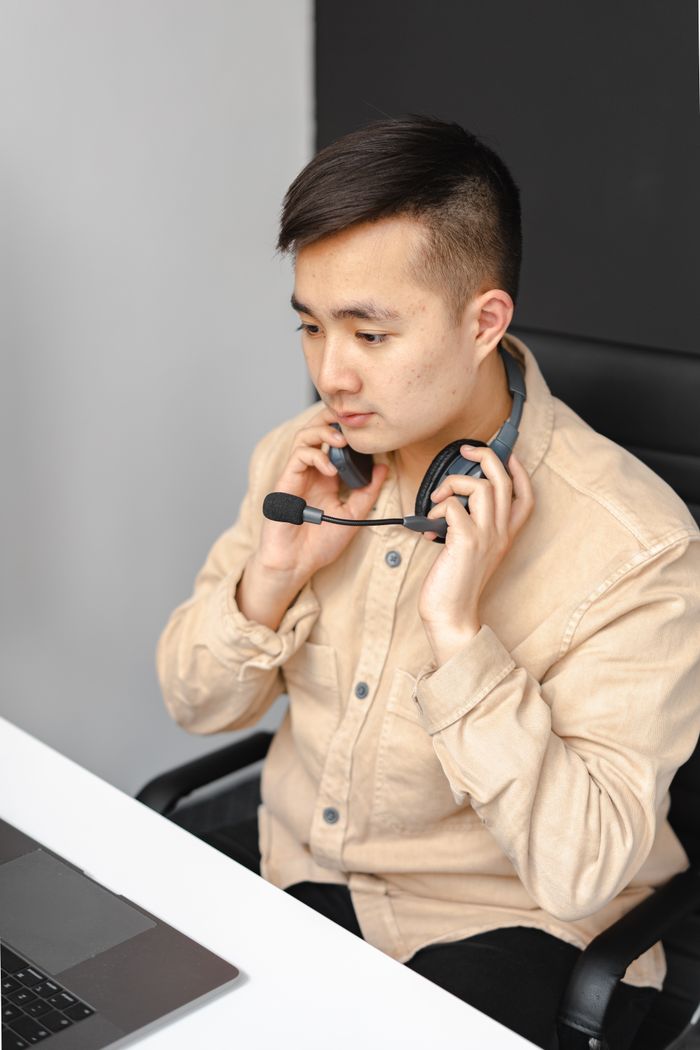 about-us Asian male technical support agent wearing a headset and working on a laptop.